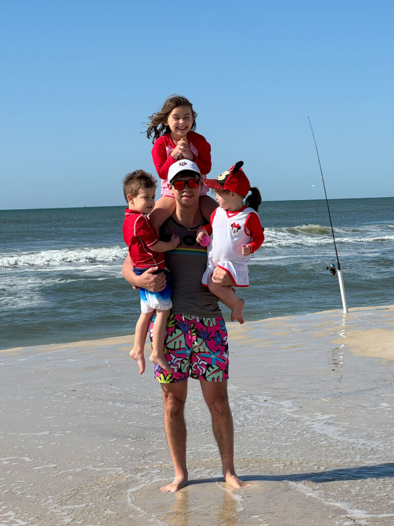 Stewart Andrews ’10 holding his children, two young girls and a young boy on the beach. 