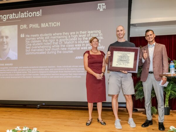 Dr. Deborah Thomas, Dr. Philip Matich, holding his award, and Kyle Easley standing on a stage