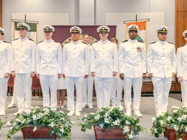 Eight new ensigns in white uniforms standing in a line on stage